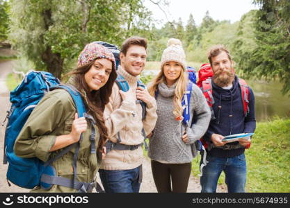 adventure, travel, tourism, hike and people concept - group of smiling friends with backpacks and map outdoors