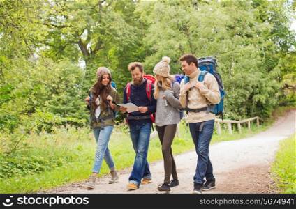 adventure, travel, tourism, hike and people concept - group of smiling friends walking with backpacks and map walking outdoors