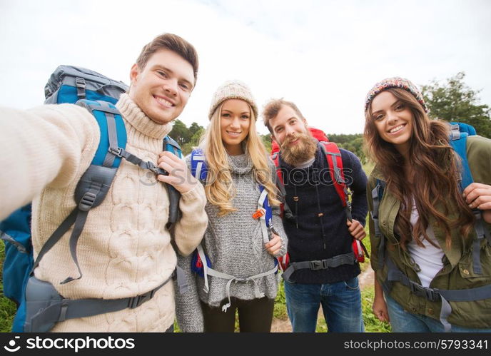 adventure, travel, tourism, hike and people concept - group of smiling friends with backpacks making selfie outdoors