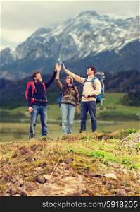 adventure, travel, tourism, hike and people concept - group of smiling friends with backpacks making high five gesture over mountains background