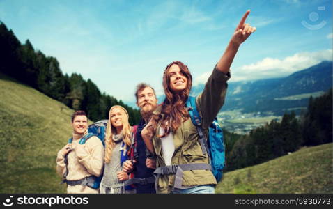 adventure, travel, tourism, hike and people concept - group of smiling friends with backpacks pointing finger over alpine hills background