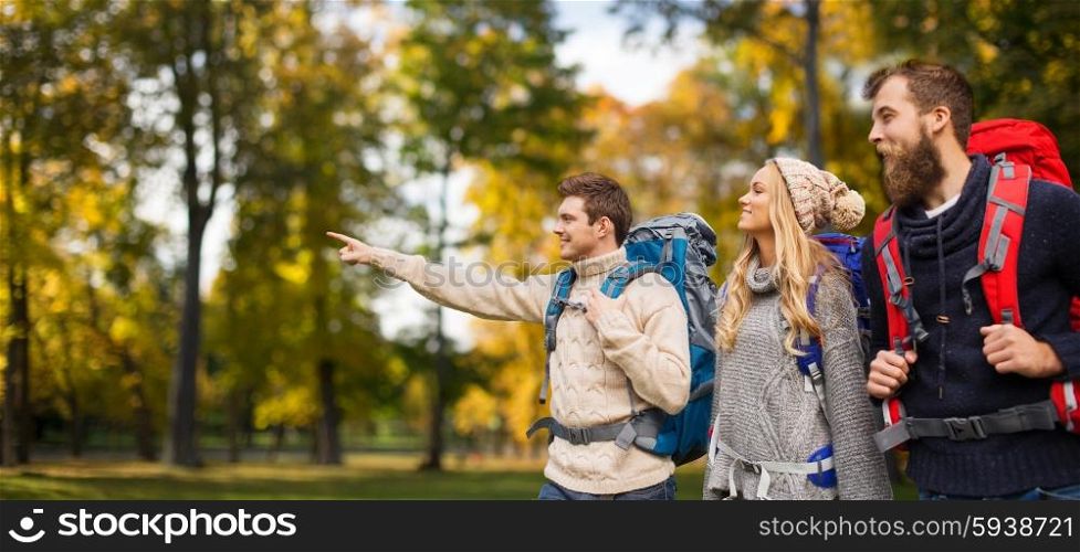 adventure, travel, tourism, hike and people concept - group of smiling friends walking with backpacks over natural background