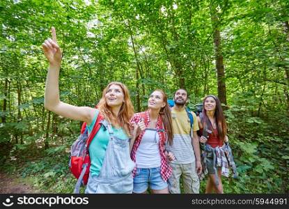 adventure, travel, tourism, hike and people concept - group of smiling friends with backpacks pointing finger up in woods