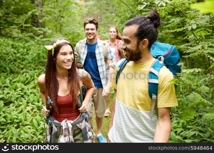 adventure, travel, tourism, hike and people concept - group of smiling friends walking with backpacks in woods