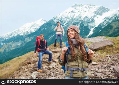 adventure, travel, tourism, hike and people concept - group of smiling friends with backpacks walking down downhill over mountains background