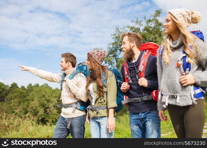 adventure, travel, tourism, hike and people concept - group of smiling friends walking with backpacks