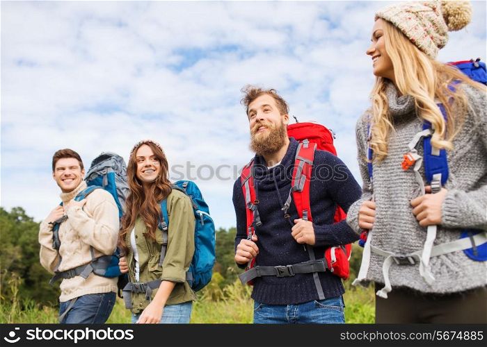 adventure, travel, tourism, hike and people concept - group of smiling friends walking with backpacks