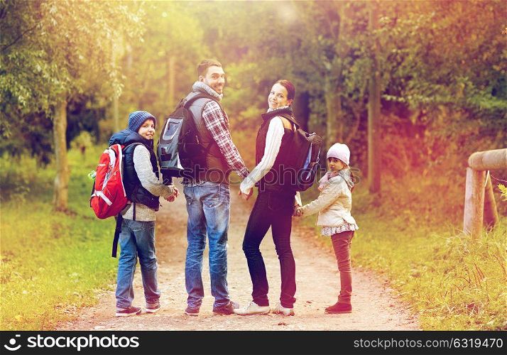 adventure, travel, tourism, hike and people concept - happy family walking with backpacks in woods and looking back. happy family with backpacks hiking walking