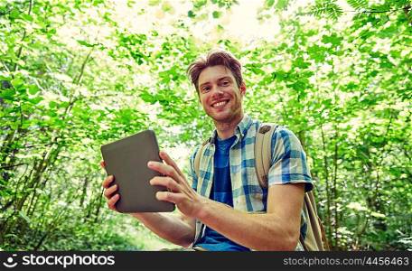 adventure, travel, tourism, hike and people concept - happy young man with backpack and tablet pc computer in woods