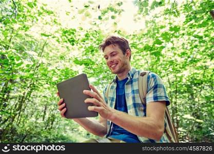 adventure, travel, tourism, hike and people concept - happy young man with backpack and tablet pc computer in woods