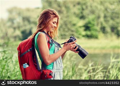 adventure, travel, tourism, hike and people concept - happy young woman with backpack and camera photographing outdoors