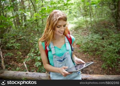 adventure, travel, tourism, hike and people concept - happy young woman with backpack and tablet pc computer sitting on fallen tree trunk in woods