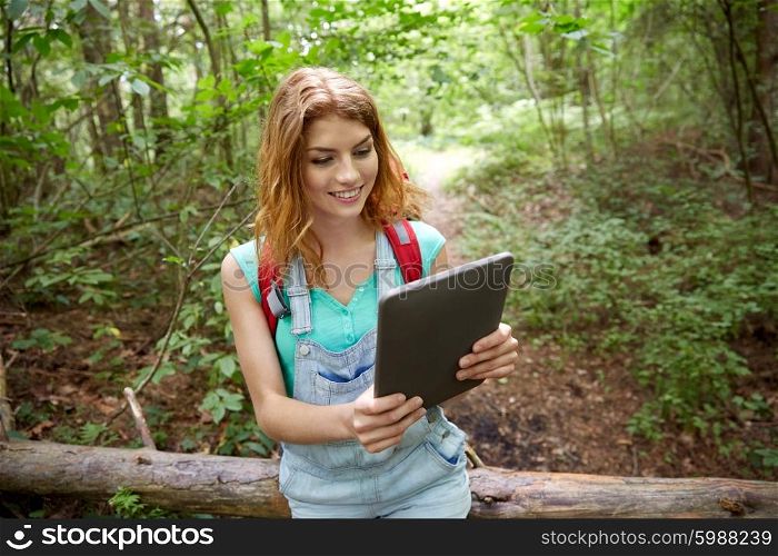 adventure, travel, tourism, hike and people concept - happy young woman with backpack and tablet pc computer sitting on fallen tree trunk in woods