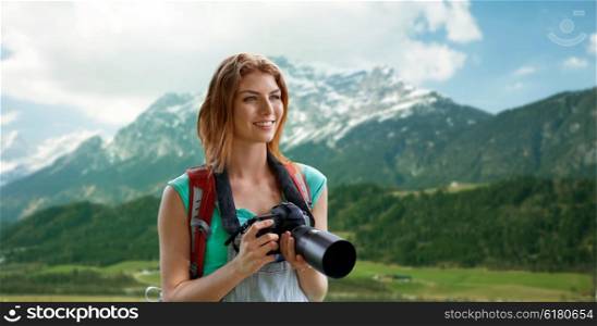 adventure, travel, tourism, hike and people concept - happy young woman with backpack and camera photographing over alps mountains background