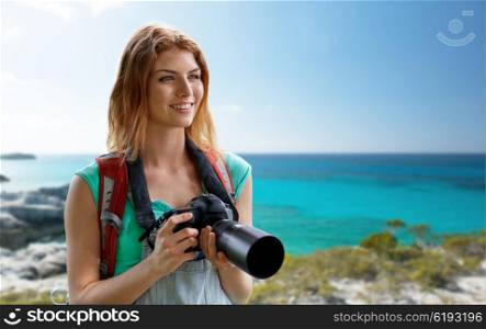 adventure, travel, tourism, hike and people concept - happy young woman with backpack and camera photographing over seashore or beach background
