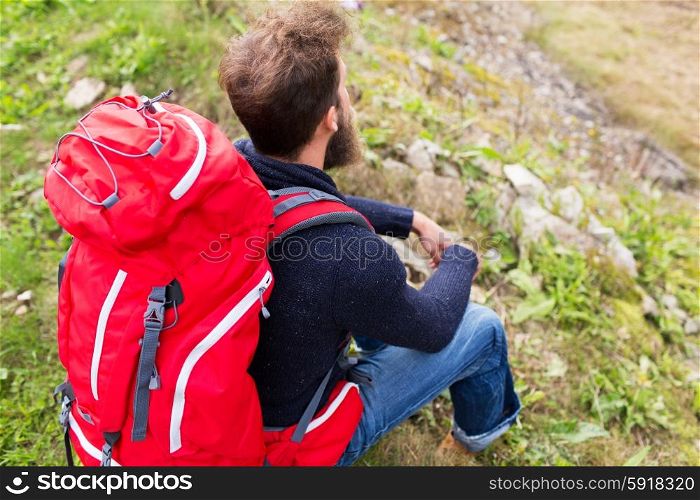 adventure, travel, tourism, hike and people concept - man hiker with red backpack sitting on ground