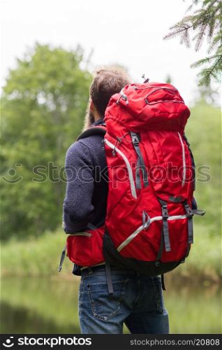 adventure, travel, tourism, hike and people concept - man hiker with red backpack standing near lake