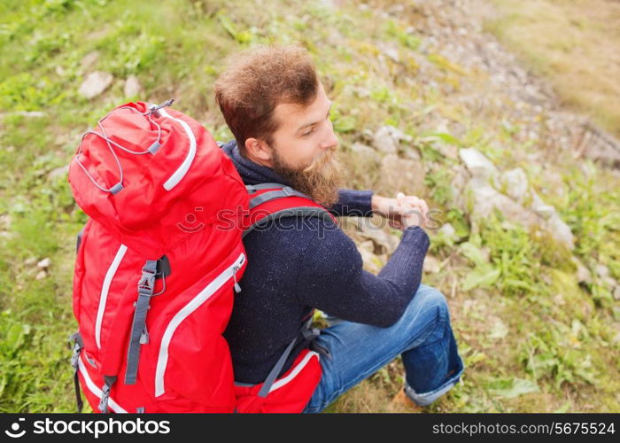 adventure, travel, tourism, hike and people concept - man with red backpack sitting on hill