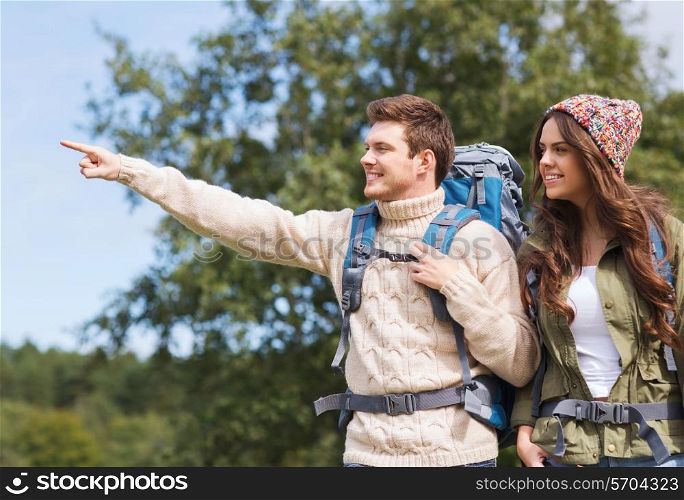 adventure, travel, tourism, hike and people concept - smiling couple of hikers with backpacks pointing finger outdoors