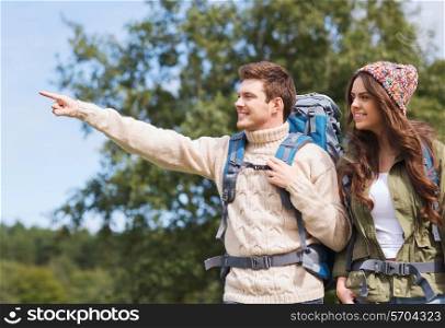 adventure, travel, tourism, hike and people concept - smiling couple of hikers with backpacks pointing finger outdoors
