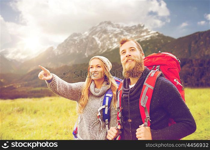 adventure, travel, tourism, hike and people concept - smiling couple walking with backpacks over alpine mountains and hills background