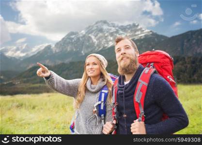 adventure, travel, tourism, hike and people concept - smiling couple walking with backpacks and pointing finger to something over mountains background