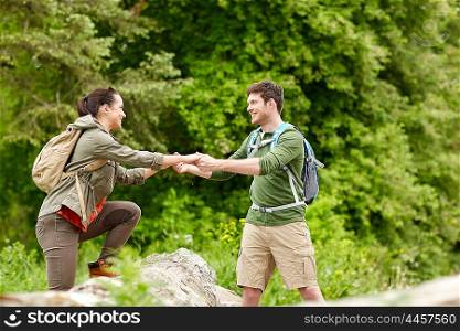 adventure, travel, tourism, hike and people concept - smiling couple with backpacks walking and climbing over fallen tree trunk in woods
