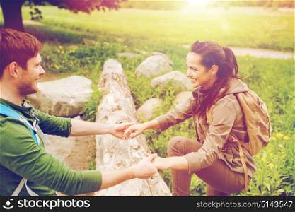 adventure, travel, tourism, hike and people concept - smiling couple with backpacks walking and climbing over fallen tree trunk in woods. smiling couple with backpacks hiking