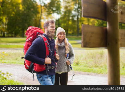 adventure, travel, tourism, hike and people concept - smiling couple with backpacks standing at signpost over autumn forest background