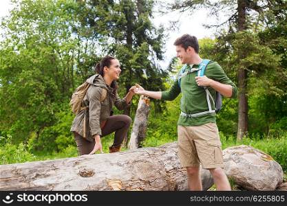 adventure, travel, tourism, hike and people concept - smiling couple with backpacks walking and climbing over fallen tree trunk in woods