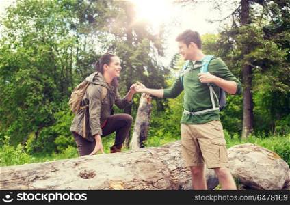 adventure, travel, tourism, hike and people concept - smiling couple with backpacks walking and climbing over fallen tree trunk in woods. smiling couple with backpacks hiking. smiling couple with backpacks hiking