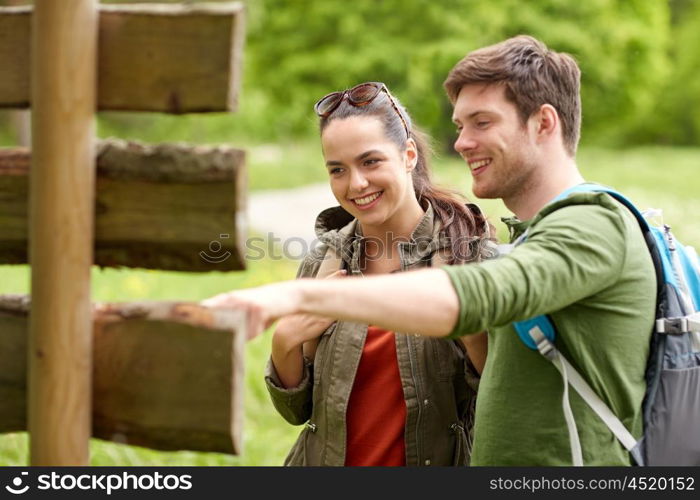 adventure, travel, tourism, hike and people concept - smiling couple with backpacks looking at signpost outdoors