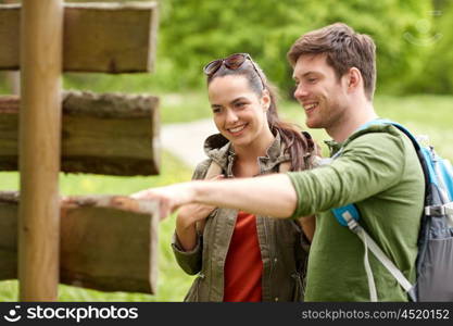 adventure, travel, tourism, hike and people concept - smiling couple with backpacks looking at signpost outdoors