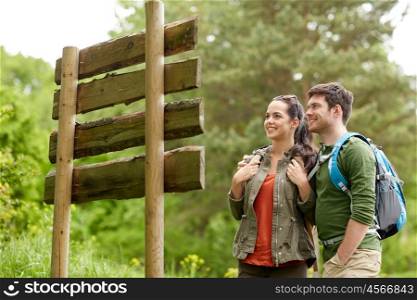 adventure, travel, tourism, hike and people concept - smiling couple with backpacks looking at signpost outdoors