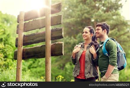 adventure, travel, tourism, hike and people concept - smiling couple with backpacks looking at signpost outdoors. smiling couple at signpost with backpacks hiking. smiling couple at signpost with backpacks hiking