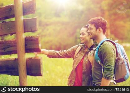 adventure, travel, tourism, hike and people concept - smiling couple with backpacks looking at signpost outdoors. smiling couple at signpost with backpacks hiking
