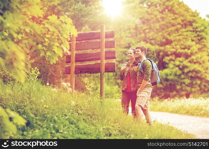 adventure, travel, tourism, hike and people concept - smiling couple with backpacks looking at signpost outdoors. smiling couple at signpost with backpacks hiking