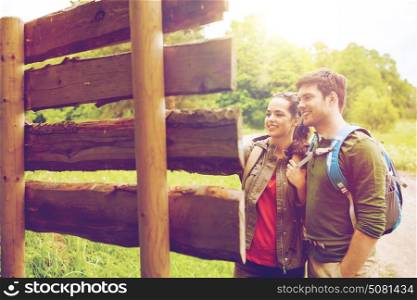 adventure, travel, tourism, hike and people concept - smiling couple with backpacks standing at signpost outdoors. smiling couple with backpacks hiking