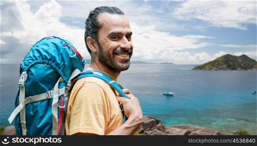 adventure, travel, tourism, hike and people concept - smiling man with backpack over background of seychelles island in indian ocean. smiling man with backpack over seychelles. smiling man with backpack over seychelles