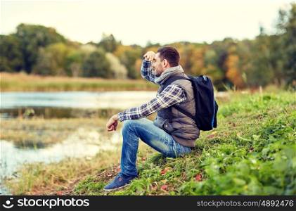 adventure, travel, tourism, hike and people concept - smiling man with backpack resting on river bank