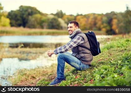 adventure, travel, tourism, hike and people concept - smiling man with backpack resting on river bank. smiling man with backpack resting on river bank