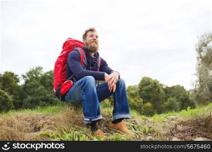 adventure, travel, tourism, hike and people concept - smiling man with red backpack sitting on ground