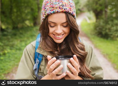 adventure, travel, tourism, hike and people concept - smiling young woman with cup and backpack in forest