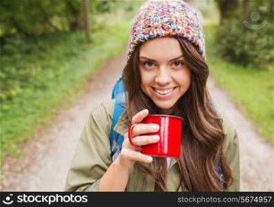 adventure, travel, tourism, hike and people concept - smiling young woman with cup and backpack in forest