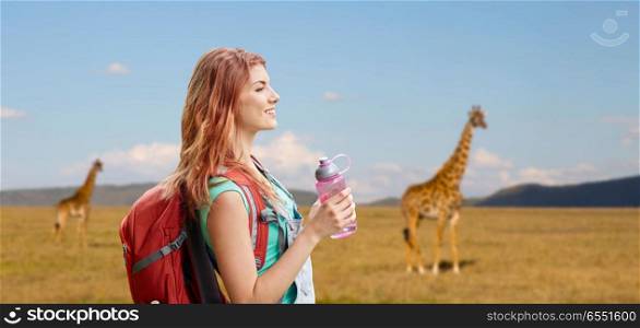 adventure, travel, tourism, hike and people concept - smiling young woman with backpack and bottle of water over giraffe in african savannah background. happy woman with backpack over african savannah. happy woman with backpack over african savannah