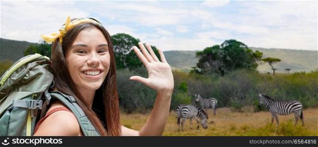 adventure, travel, tourism, hike and people concept - smiling young woman with backpack over zebras in african savannah background. happy woman with backpack over savannah