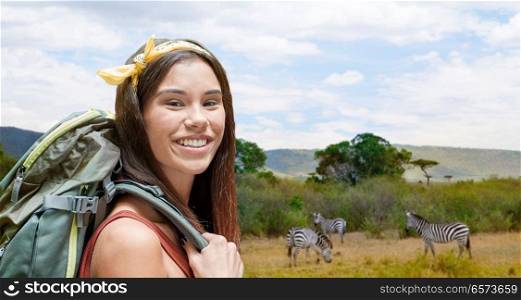 adventure, travel, tourism, hike and people concept - smiling young woman with backpack over zebras in african savannah background. happy woman with backpack over savannah