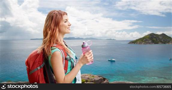 adventure, travel, tourism, hike and people concept - smiling young woman with backpack and bottle of water over background of seychelles island in indian ocean. happy woman with backpack over seychelles island