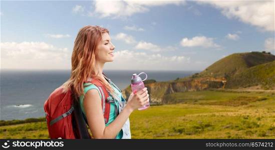 adventure, travel, tourism, hike and people concept - smiling young woman with backpack and bottle of water over big sur coast of california background. smiling woman with backpack on big sur coast