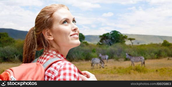 adventure, travel, tourism, hike and people concept - smiling young woman with backpack over zebras in african savannah background. happy woman with backpack over african savannah